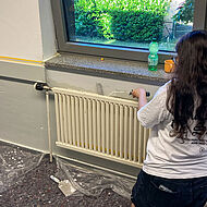 Eine Schülerin einer Dortmunder Schule kniet auf Malervlies bei einem Projekt zur Berufsorientierung und probiert sich im Malerhandwerk selbst am Pinsel aus