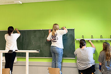 Vier Schülerinnen einer Dortmunder Schule streichen die Wand ihres Klassenzimmers grün
